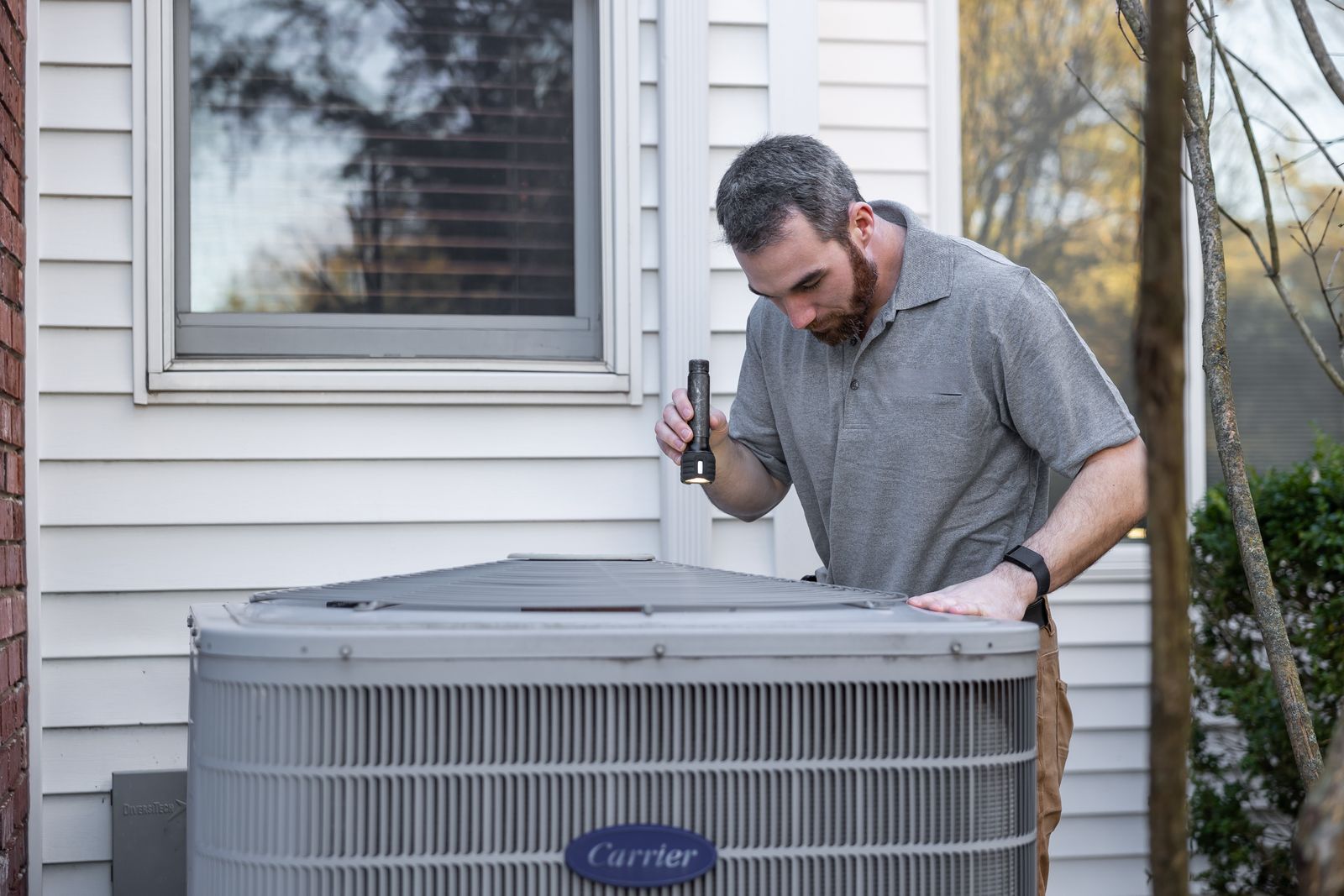 DUCTS technician inspecting an outdoor HVAC condenser unit during a Birmingham AL maintenance tune-up